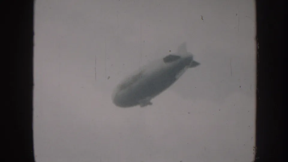 The blimp remains high in a pale cloudy sky, softly rendered by the 1958 8mm home-movie scan.