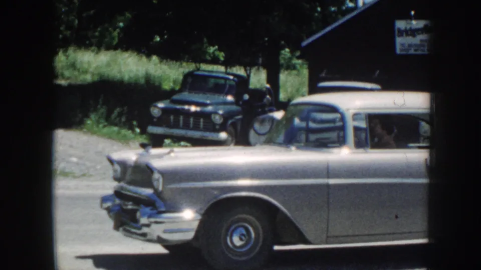 Side view of the silver sedan in 1958 Nebraska passing a dark pickup, with chrome trim and whitewall tire visible.