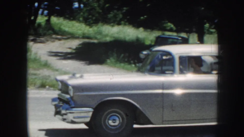 Silver 1950s sedan continues along the rural Nebraska road, partly cropped as it passes the camera.