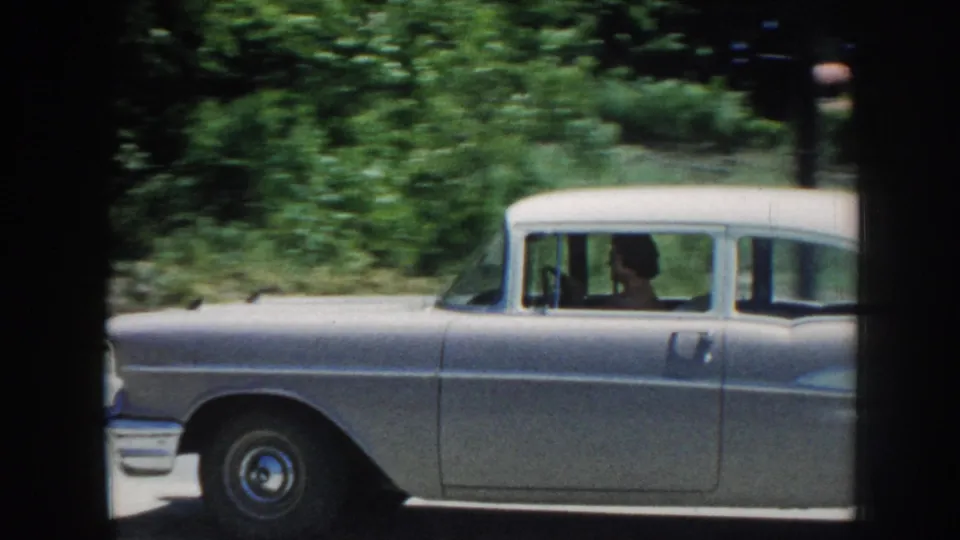 The silver sedan moves out of frame in rural Nebraska, with the driver silhouette visible through the side window.