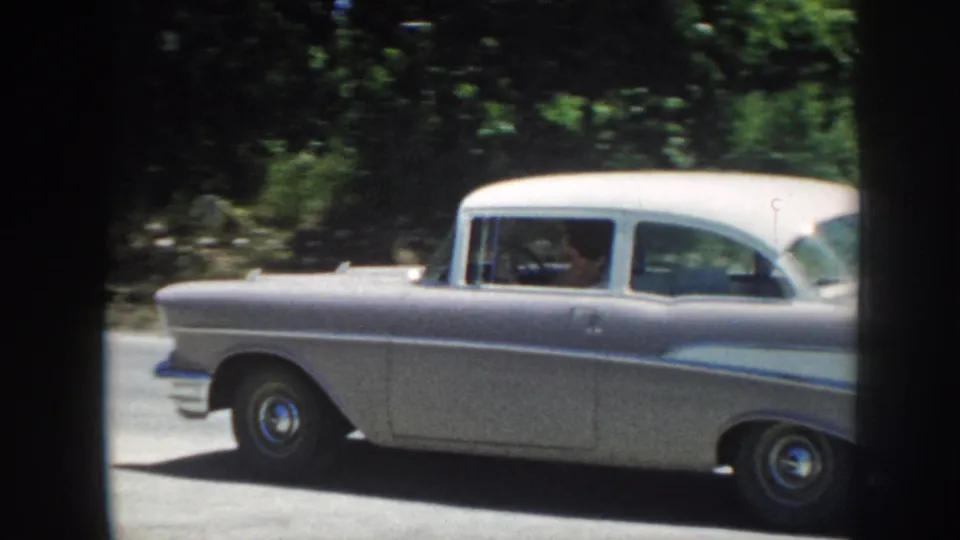 A silver midcentury sedan drives past on a sunny road in footage identified as 1958 Nebraska.