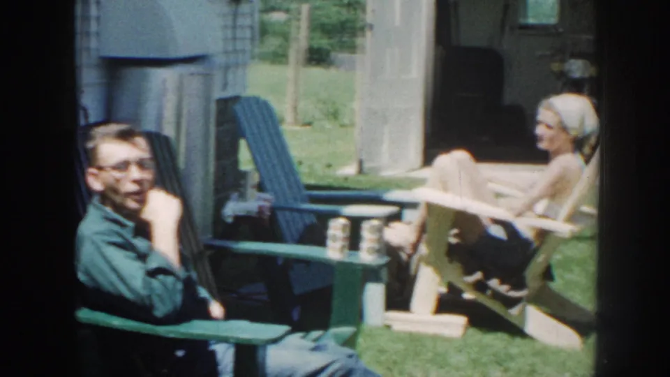 A man and a woman sit in separate lawn chairs near a small table on a sunny Nebraska yard, consistent with the 1958 metadata.