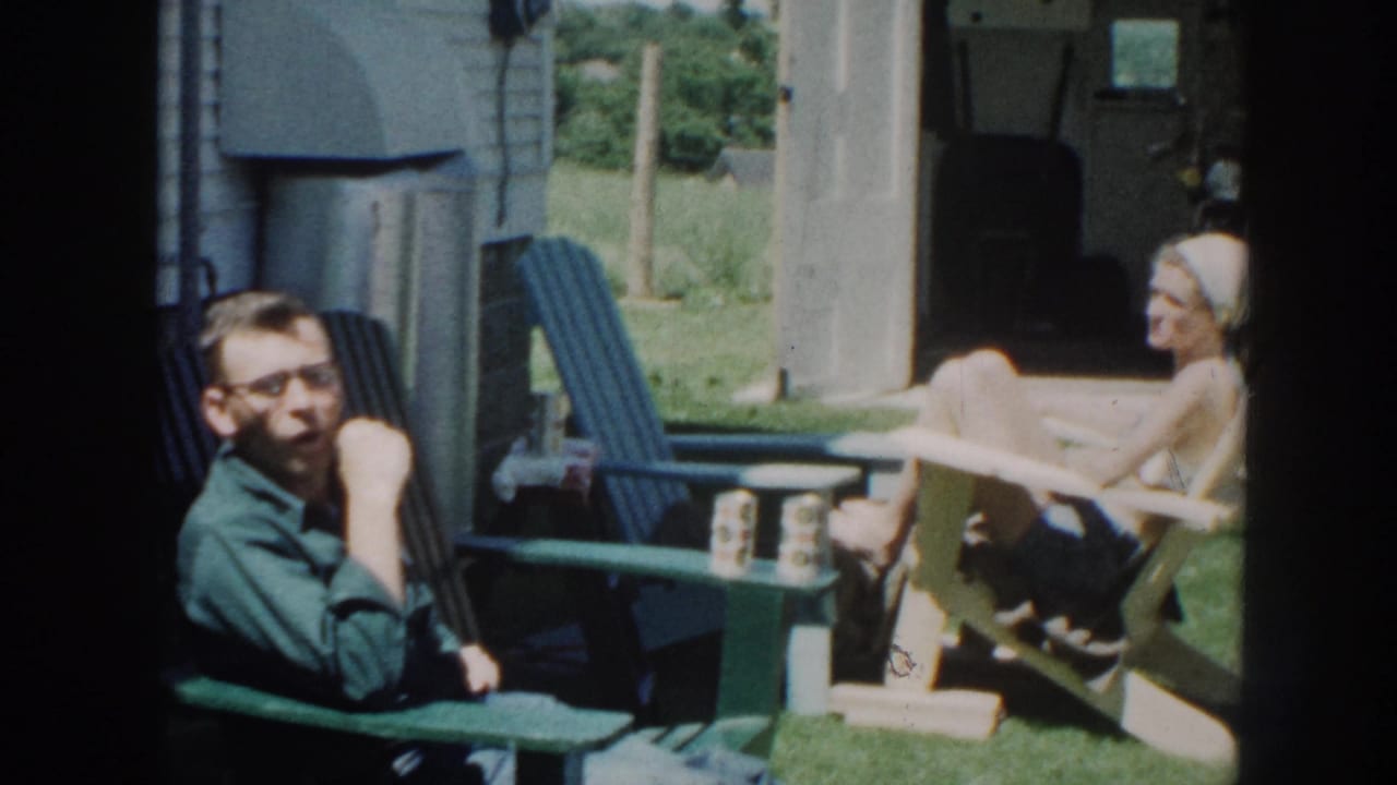 Man in glasses sits in a green chair near a woman reclining in a backyard chair.