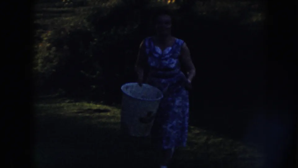 Near the end of the 1958 Nebraska clip, the woman carries the bucket closer to camera, partly silhouetted by dusk shadows.