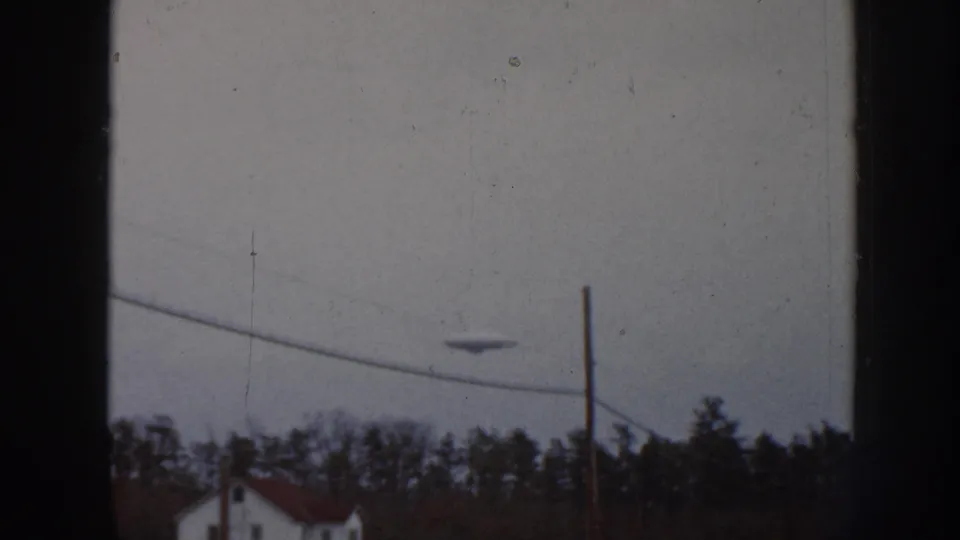 1958 Nebraska 8mm frame showing the dark object above a rural treeline, with a wire crossing the lower sky and a pole at right.