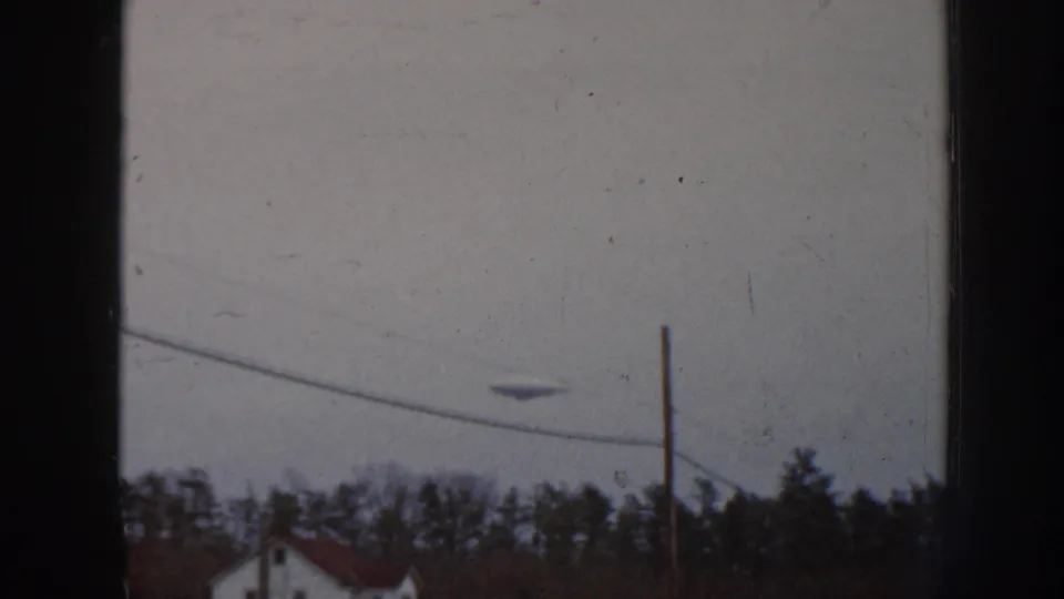 1958 Nebraska 8mm frame with a dark disc-like object in the pale sky above trees, a utility pole, sloping wire, and house roofline.