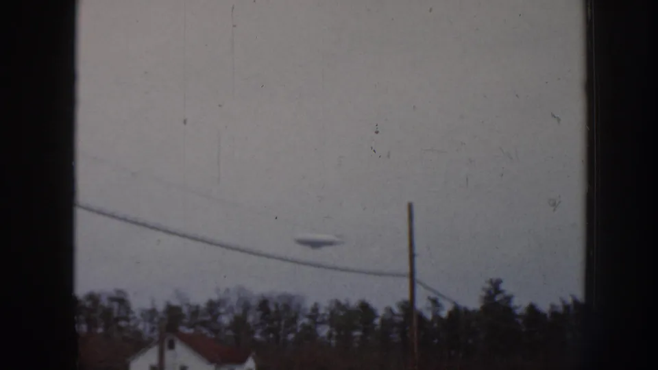 1958 Nebraska 8mm frame showing a disc-like object over utility lines, bare trees, and a rural house viewed through dark framing.