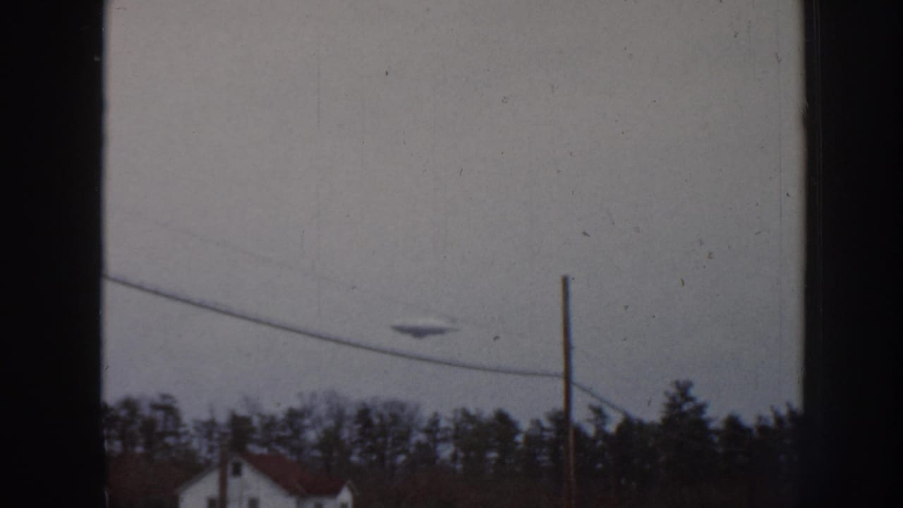 1958 Nebraska 8mm frame with a disc-like object in an overcast sky near a utility wire, pole, treeline, and distant house.