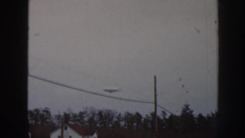 1958 Nebraska 8mm frame showing the aerial object above a sloping utility wire, with bare trees and a partial house below.