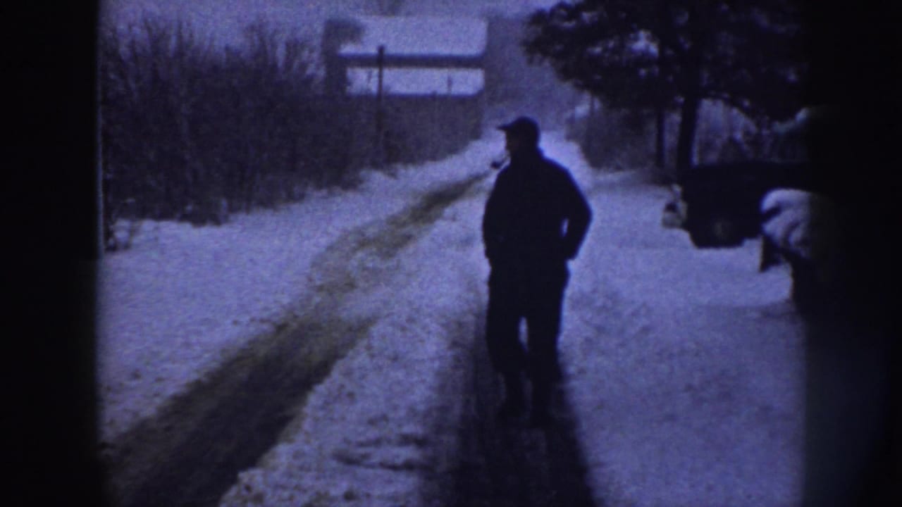 Lone man in dark winter clothing walking away along a snow-covered rural road.