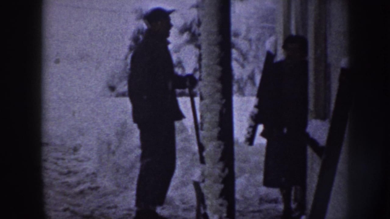 In 1958 Nebraska home-movie footage, two bundled figures stand in a snowy yard area, with one person holding a shovel.