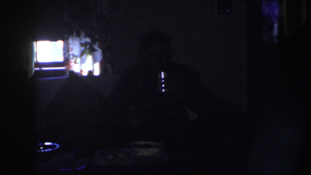 Dark room with a seated adult at a table near a bright rectangular glow.