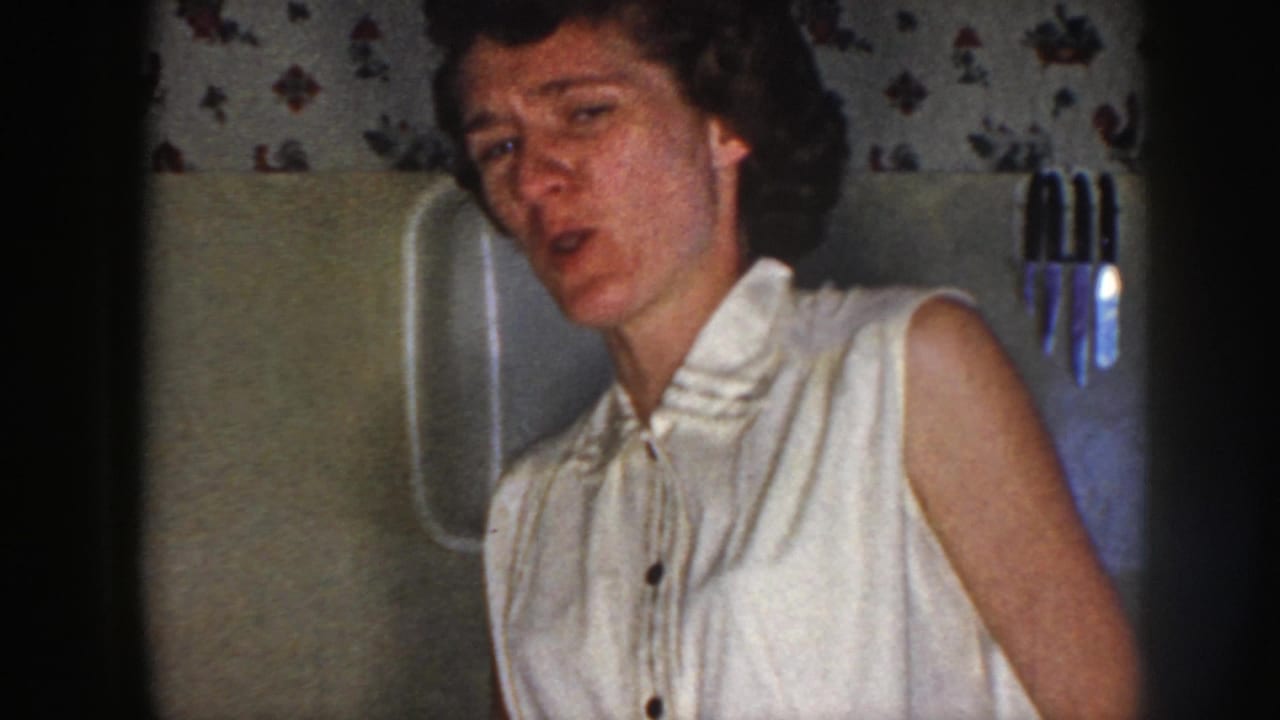 Woman in a white sleeveless blouse seated or leaning in a bathroom interior.