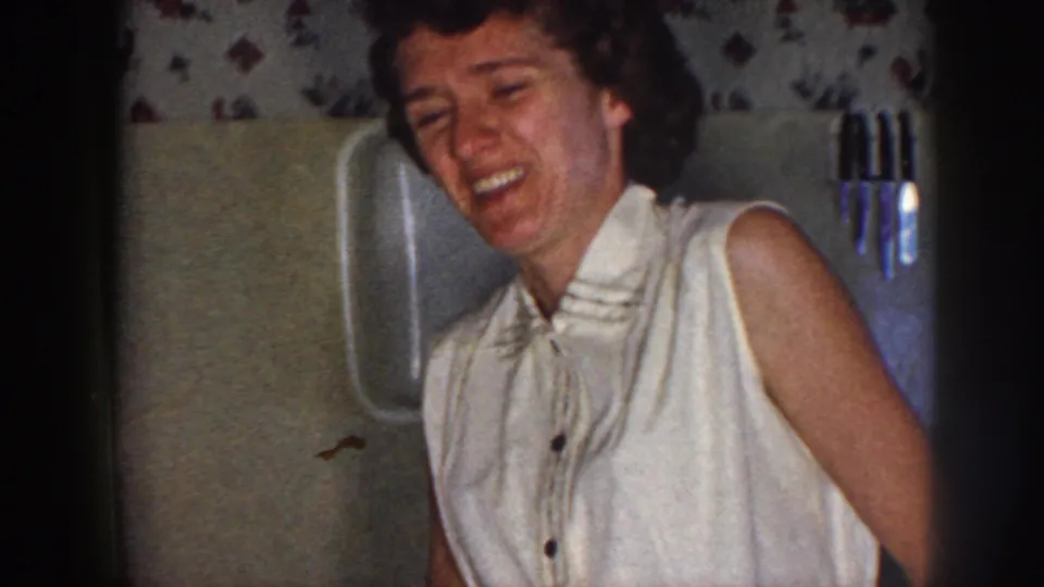 Adult woman laughs heartily in a private Nebraska bathroom captured on 8mm film in 1958.