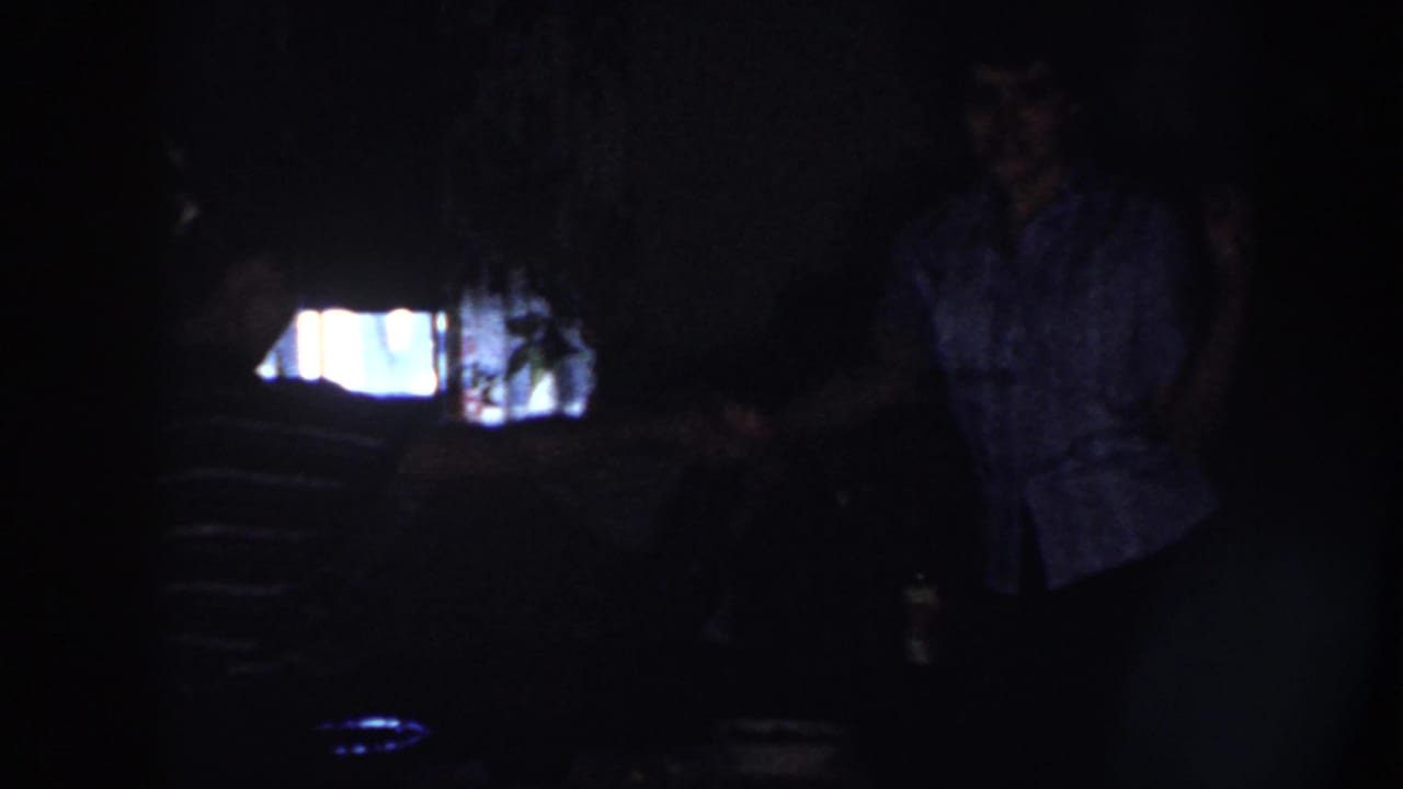 Two people stand in a dark room near a bright rectangular light source.