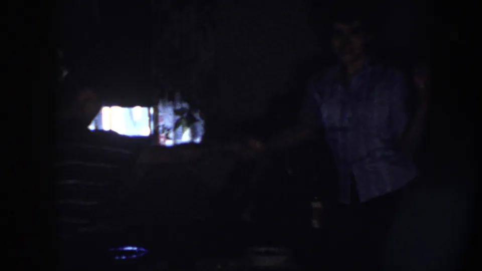 In Nebraska 1958 home-movie footage, a young couple stands in a dim private interior with their bodies partly silhouetted.