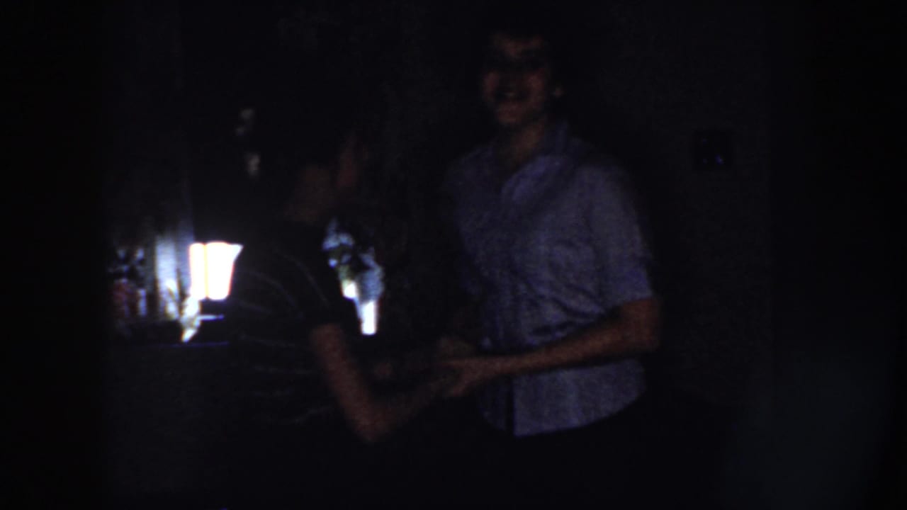 A young couple dances in a dim room, partly lit from behind.