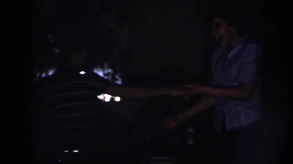 A young couple holds hands while dancing in a low-lit Nebraska home-movie scene from 1958.