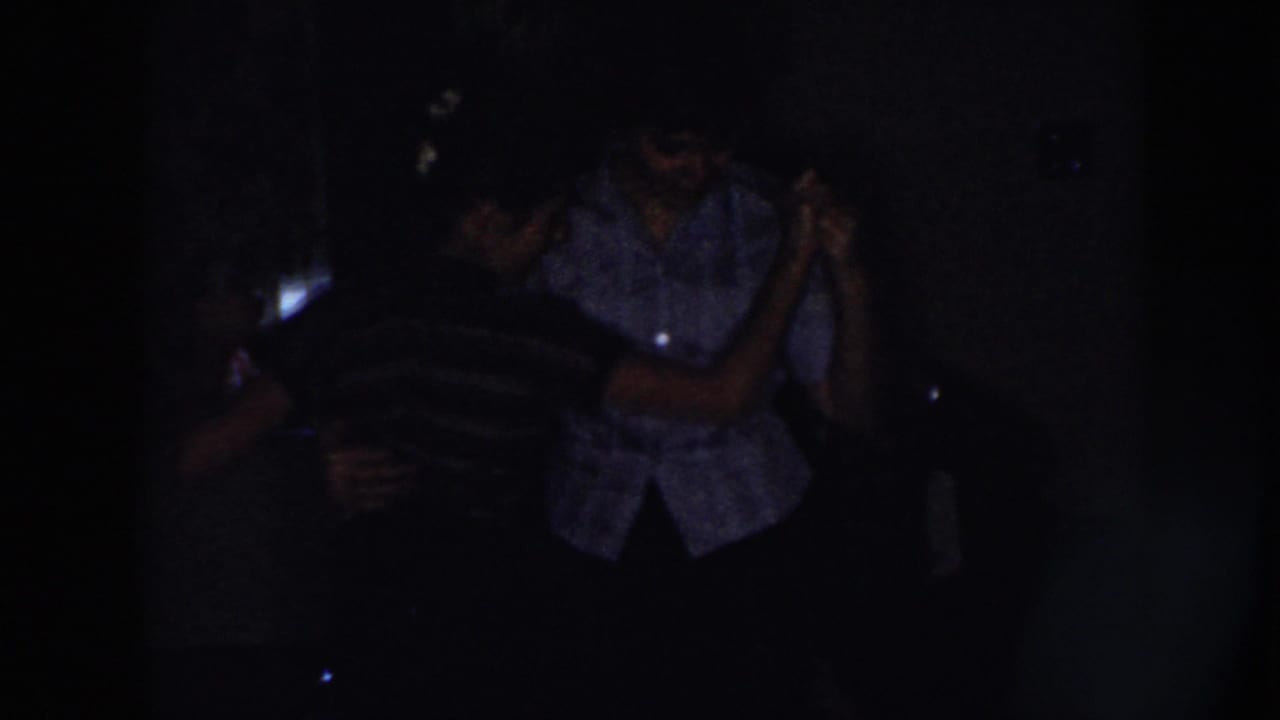 Two adults dancing closely in a very dark interior.