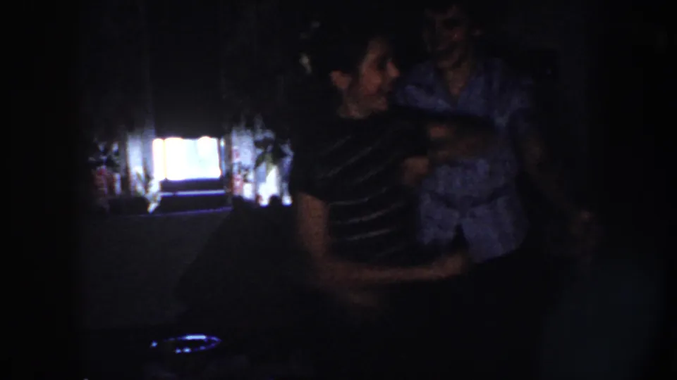 The dancing couple is seen more closely in the dark interior, with a glowing screen or window behind them.