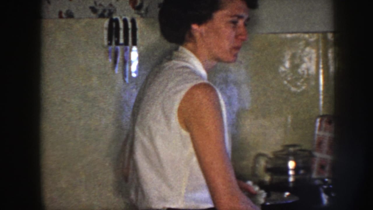 Woman in profile at a kitchen stove with cookware and wall knives nearby.