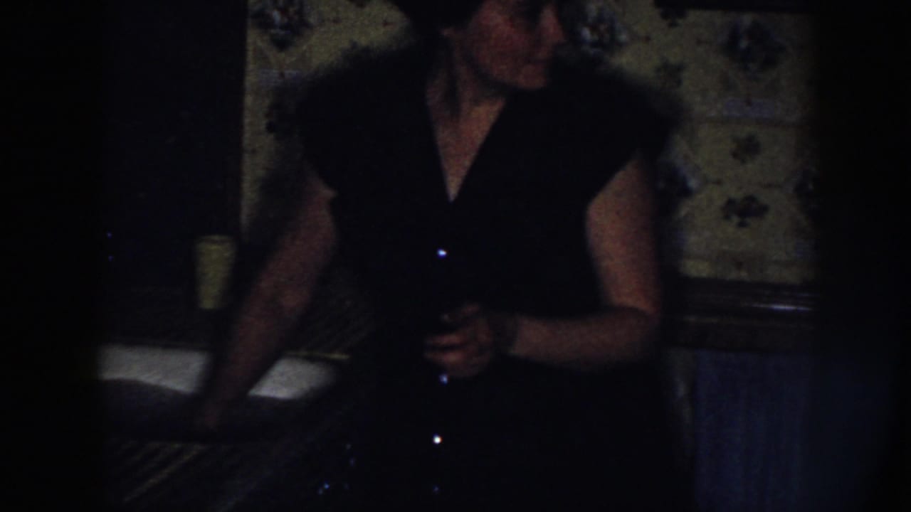 Woman in a dark dress stands at a kitchen sink in a dim room.