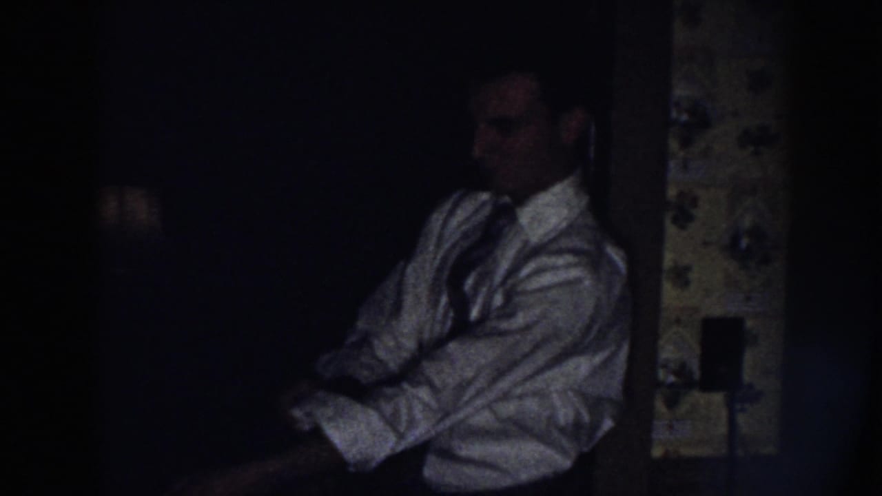 Man in a white shirt and tie adjusts a sleeve in a dark interior.