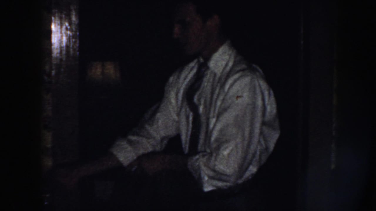 Dim kitchen view with a man in a white shirt and tie near a dark work area.