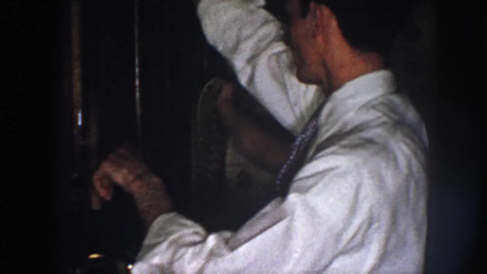 Close side view of the man in a white shirt and tie raising his arm while adjusting clothing in the dim kitchen.