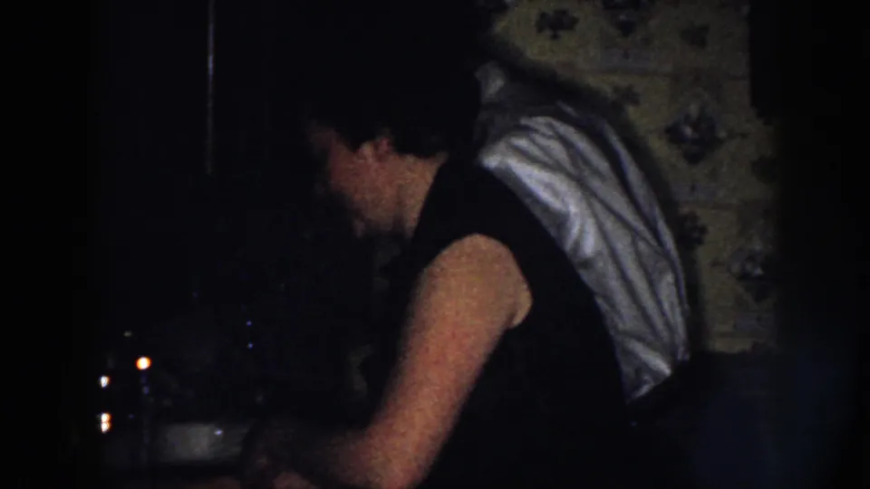 A woman in a dark sleeveless dress stands at the kitchen work area while the man in a white shirt remains nearby.