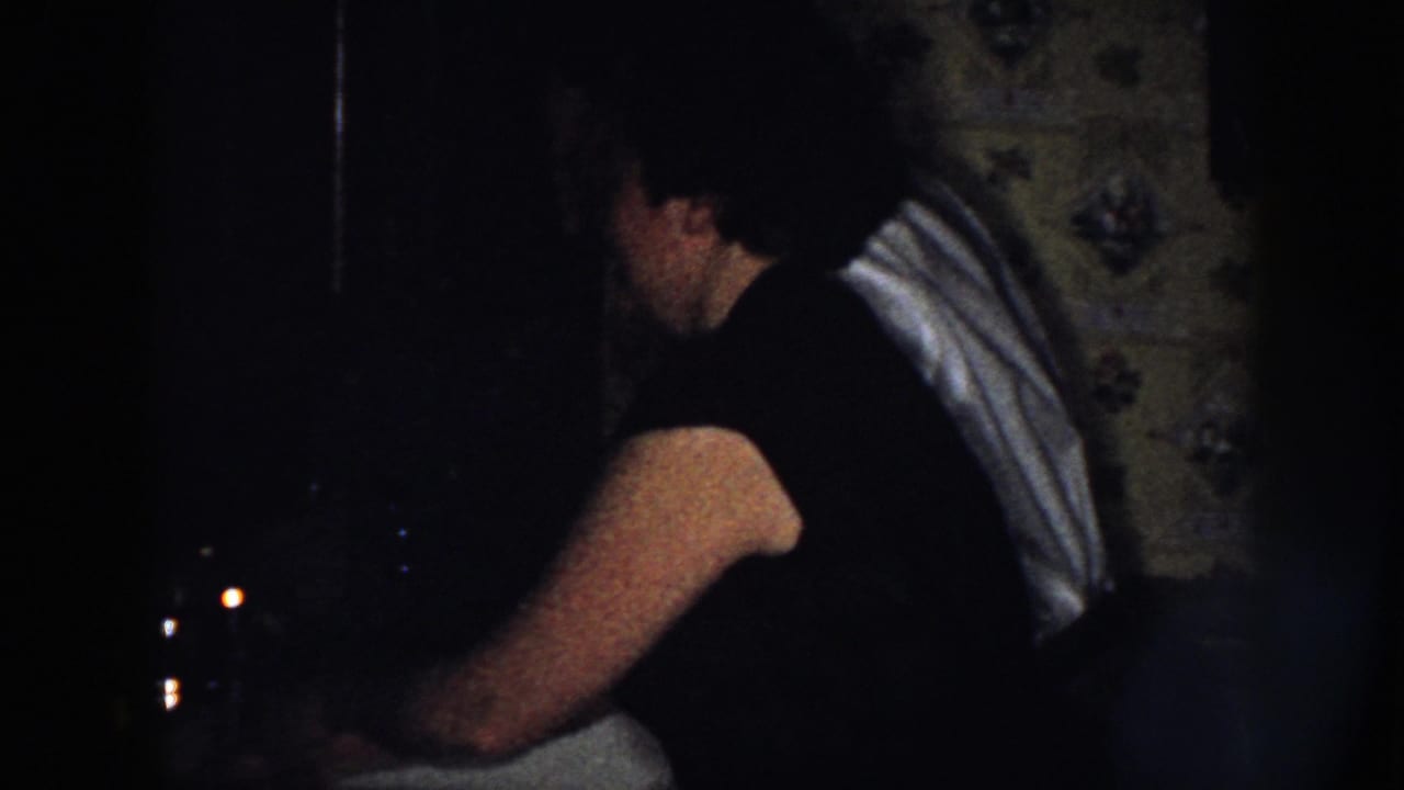 Woman seen from behind at a dim kitchen sink with a light shawl over one shoulder.
