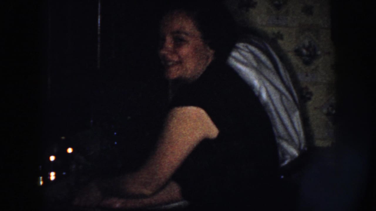 Woman turns toward the camera while standing by the sink in a dark interior.