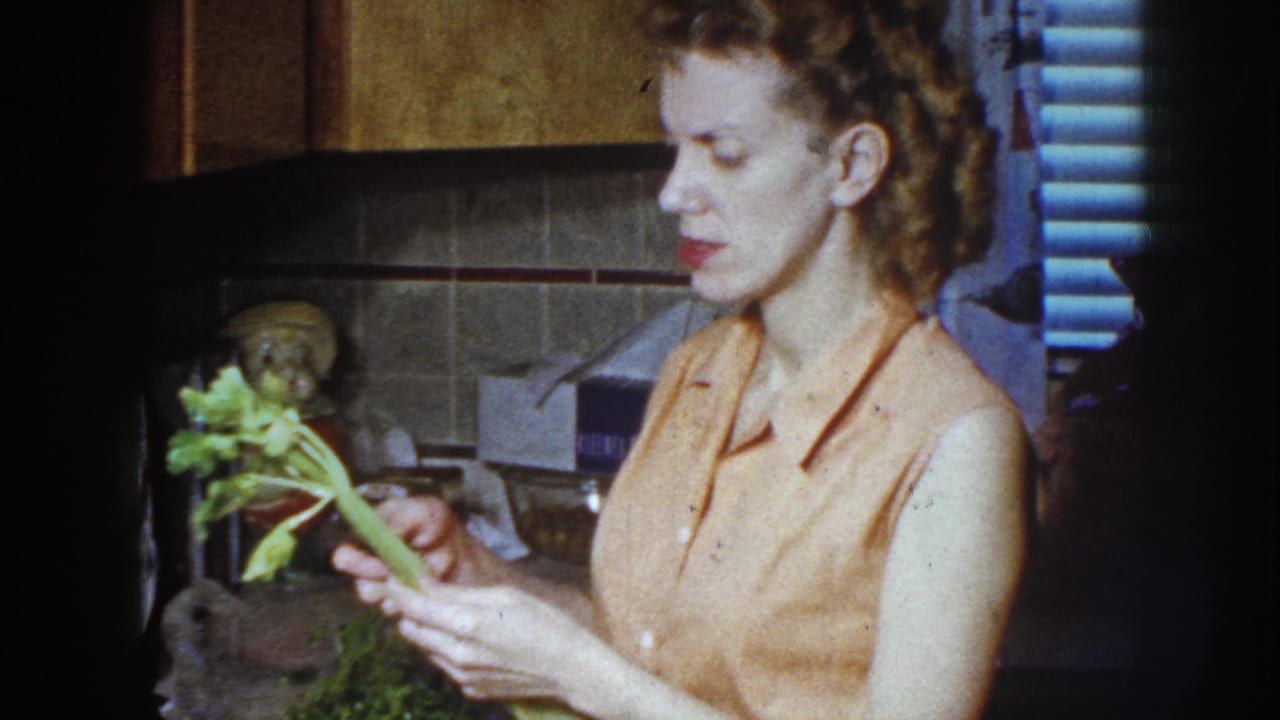 Woman in a kitchen holds celery and a paring knife near a tiled backsplash.