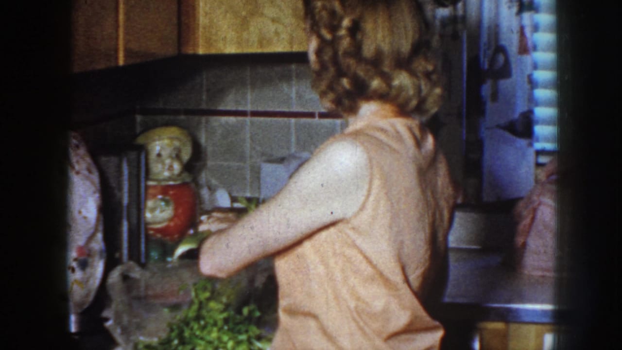 Woman turned toward a kitchen counter with celery and countertop items visible.