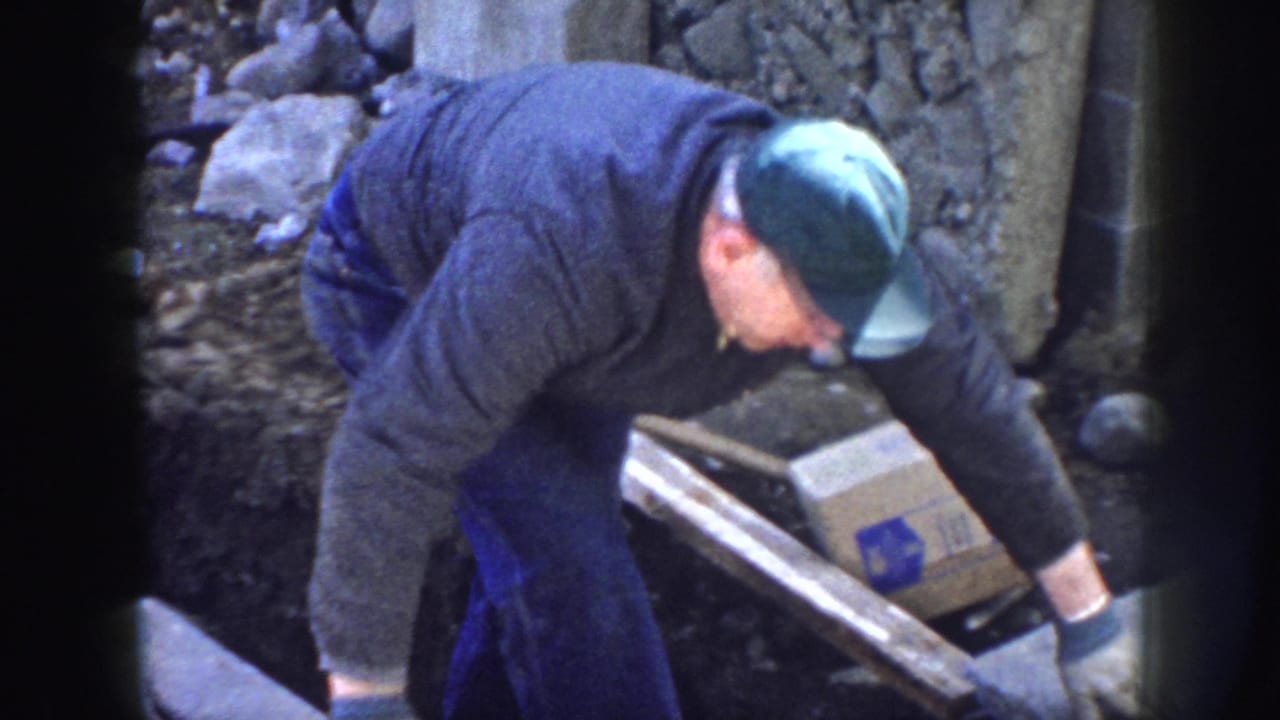 Man in a green cap bends over materials at a construction site.