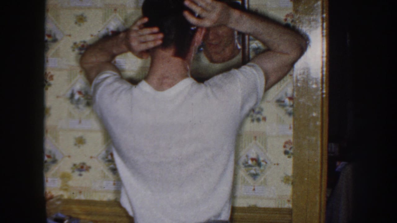 Young man raises both hands to his head while looking into a wall mirror.