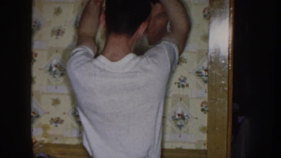 From behind, the young man keeps both arms raised as he works on his hair in a modest 1958 Nebraska home interior.