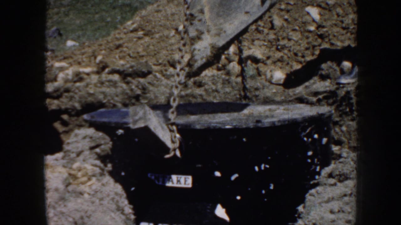 Black utility vault suspended over a trench by chains, with dirt and rocks around it.