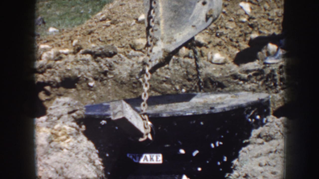 Chain rigging lowers a dark utility vault into a rough trench.