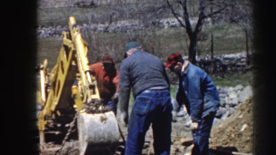 Three adult men in rural Nebraska, 1958, stand near a yellow backhoe and dirt pile in an outdoor work area.