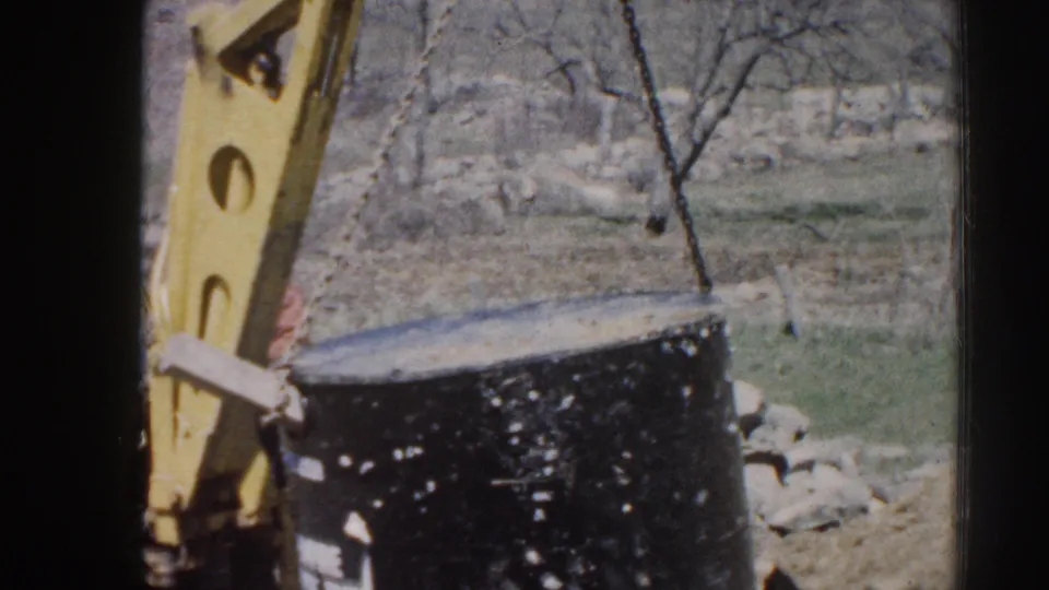 Near the end of the clip, the black cylinder hangs from a chain beside the yellow backhoe in a rural Nebraska work setting.