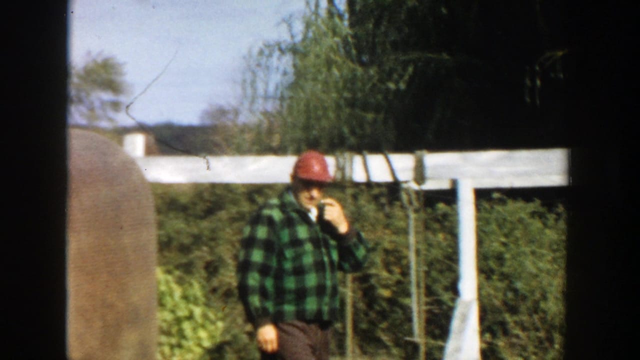 Man in red cap and plaid shirt stands near a white fence.