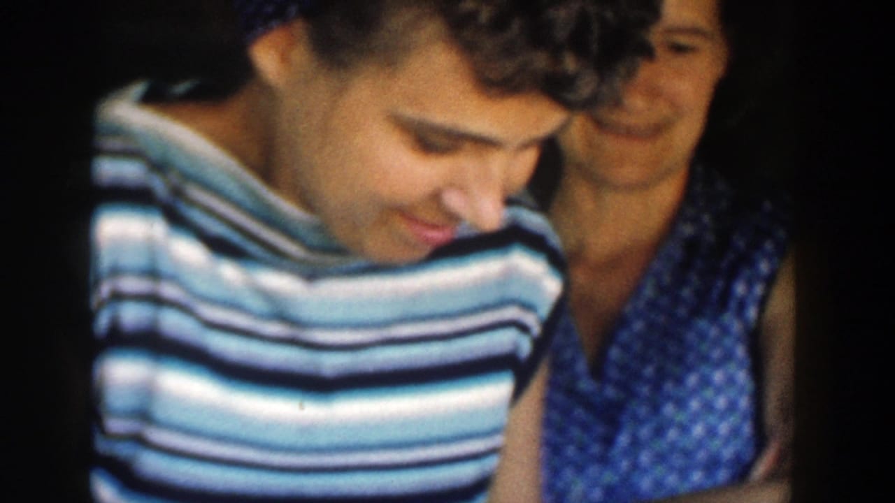 In a 1958 Michigan interior, a woman in a striped sleeveless top looks down while another woman smiles from behind her shoulder.