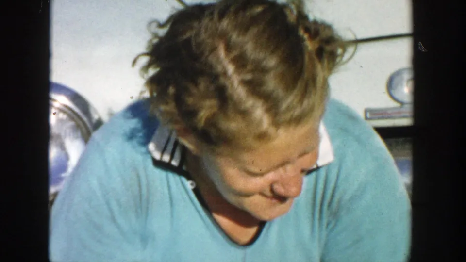 A close 1958 Michigan frame shows the woman looking down shyly beside the car, with part of the vehicle behind her.