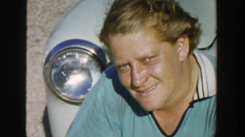 A close frame from the 1958 Michigan clip shows the woman smiling beside the car's front end and chrome headlight.