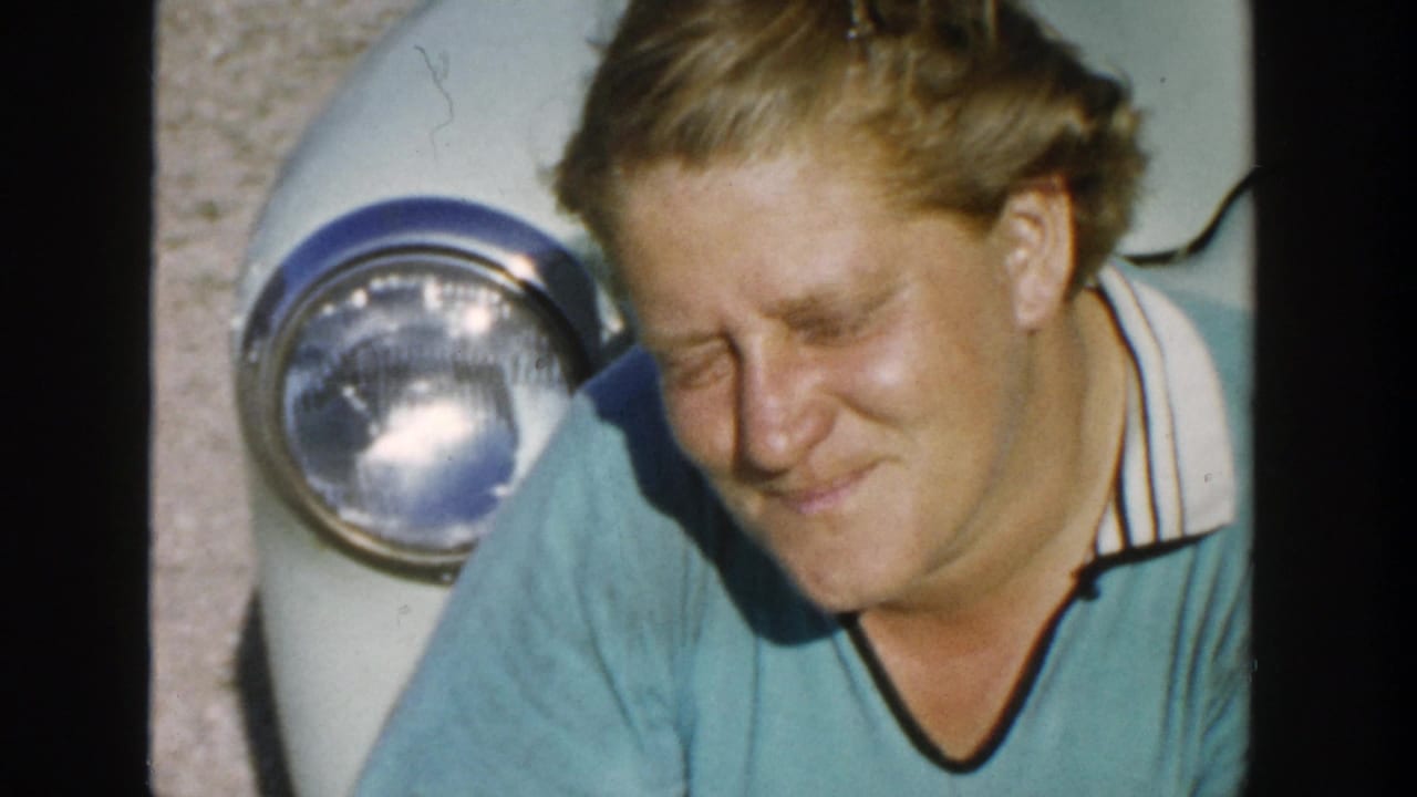 Woman in a green shirt squinting beside a light-colored car headlight.