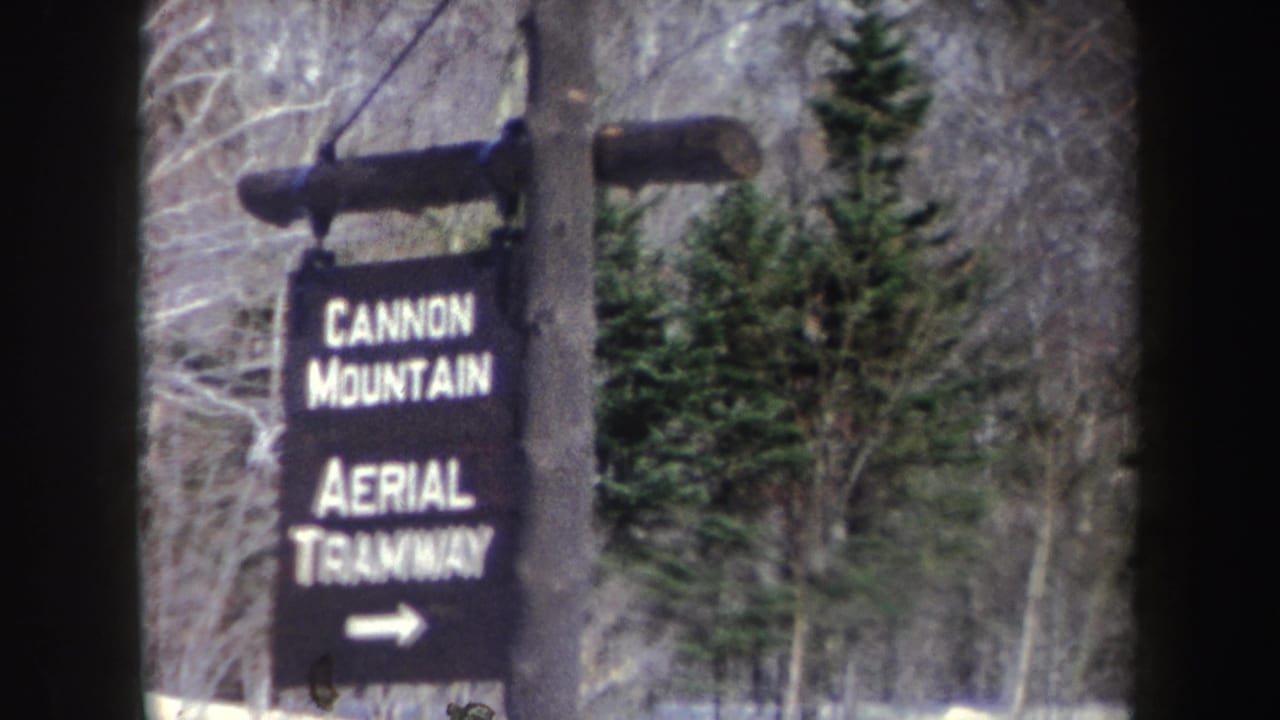 1962 8mm frame of a Cannon Mountain Aerial Tramway sign with a right arrow in a snowy forest setting.