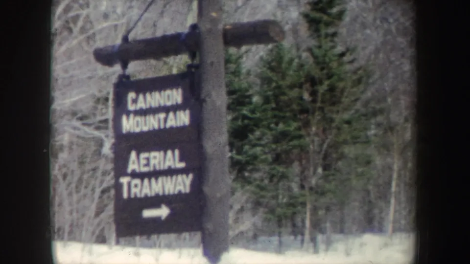 A slightly shifted 8mm view shows the Cannon Mountain Aerial Tramway sign against snow, bare branches, and evergreen trees.