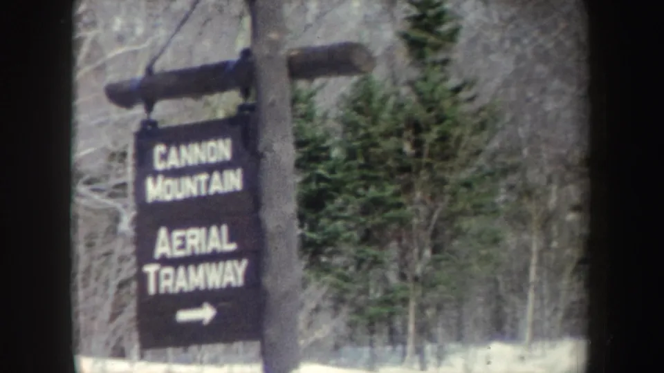 Vintage 8mm view of the Cannon Mountain Aerial Tramway sign against snow, evergreens, and leafless winter trees.