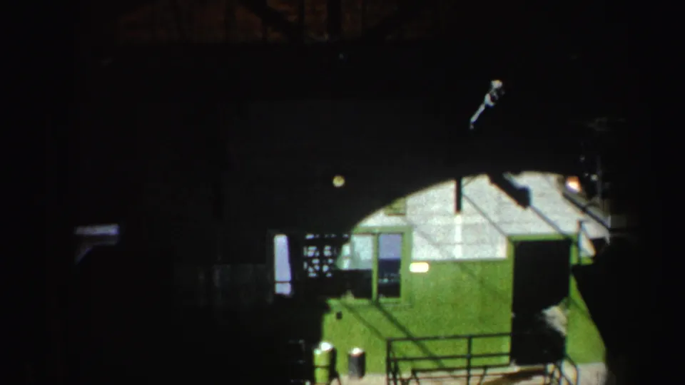 1962 New York 8mm view of a green industrial machine component moving through a shadowed interior structure.